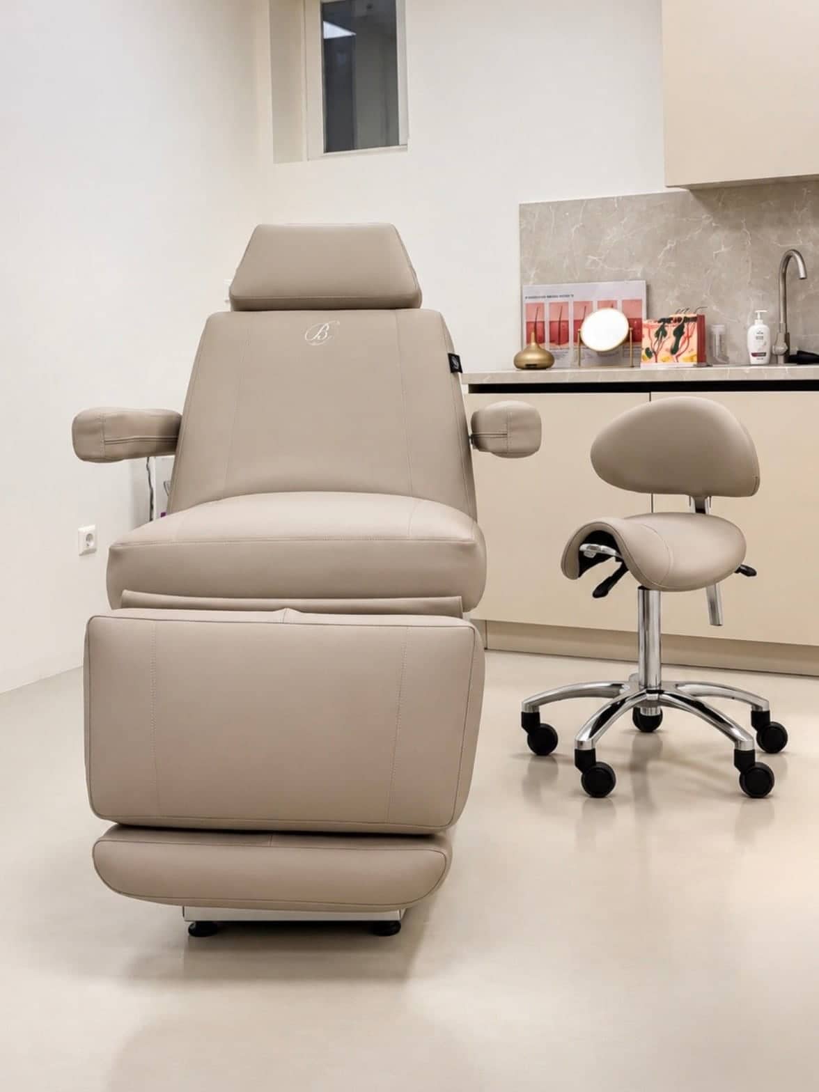 De behandelkamer van Clinic Noord met een crèmekleurige behandelstoel, een krukje en de balie